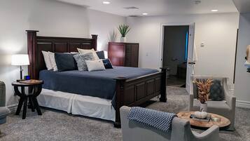 A bedroom with a large bed, a bedside table, a chair, and a small table with a lamp.