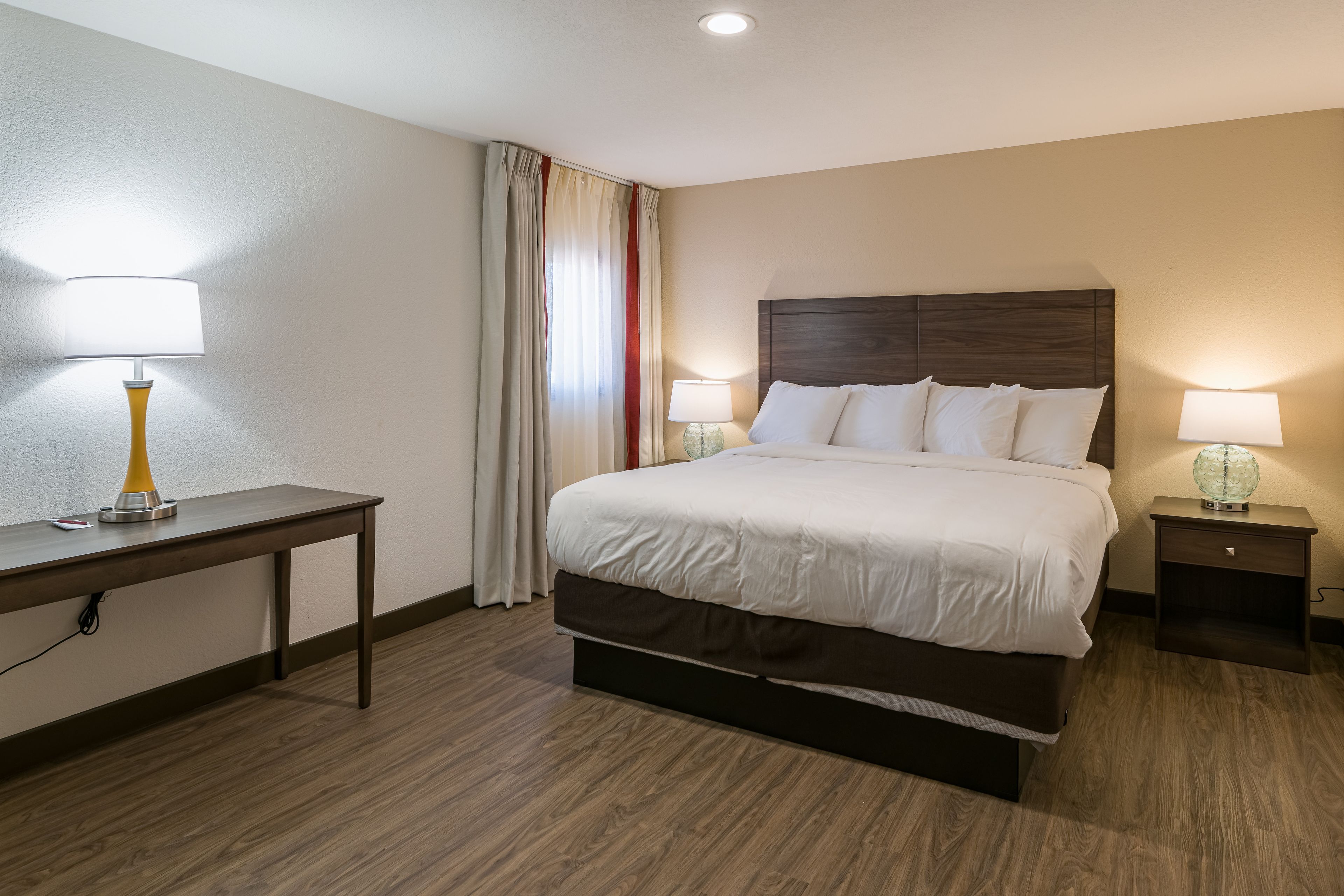 A hotel room with a bed, bedside tables, a desk, and a lamp.