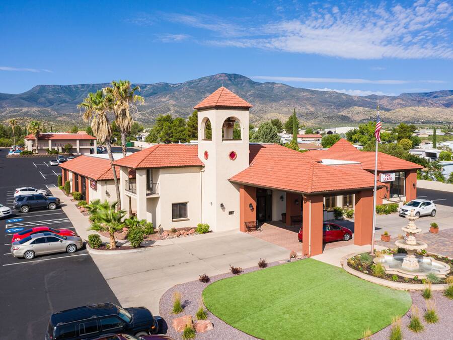 A hotel with a red-tiled roof, a bell tower, and a parking lot with several cars.