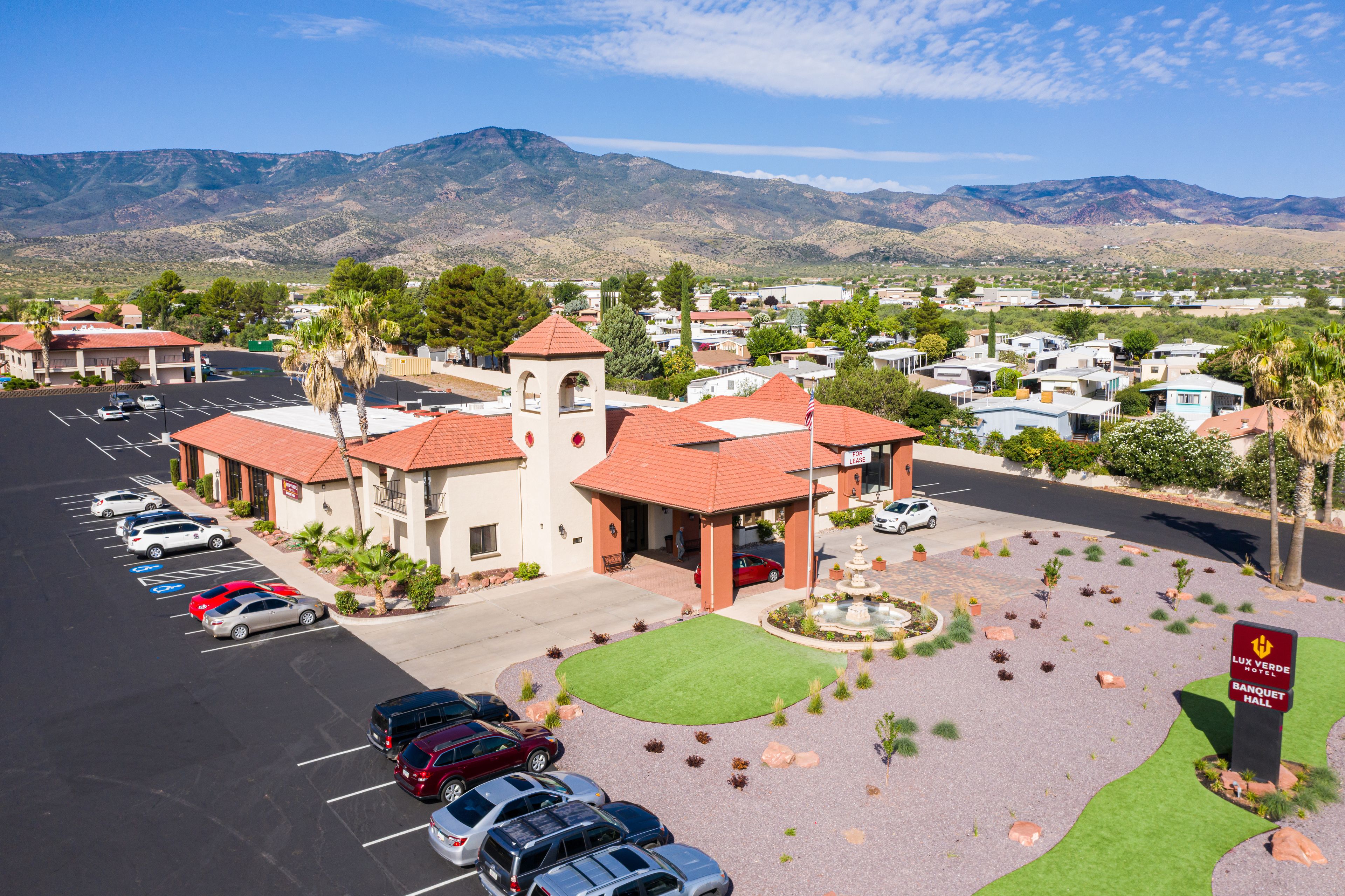 Un hotel con aparcamiento, una fuente y montañas al fondo.