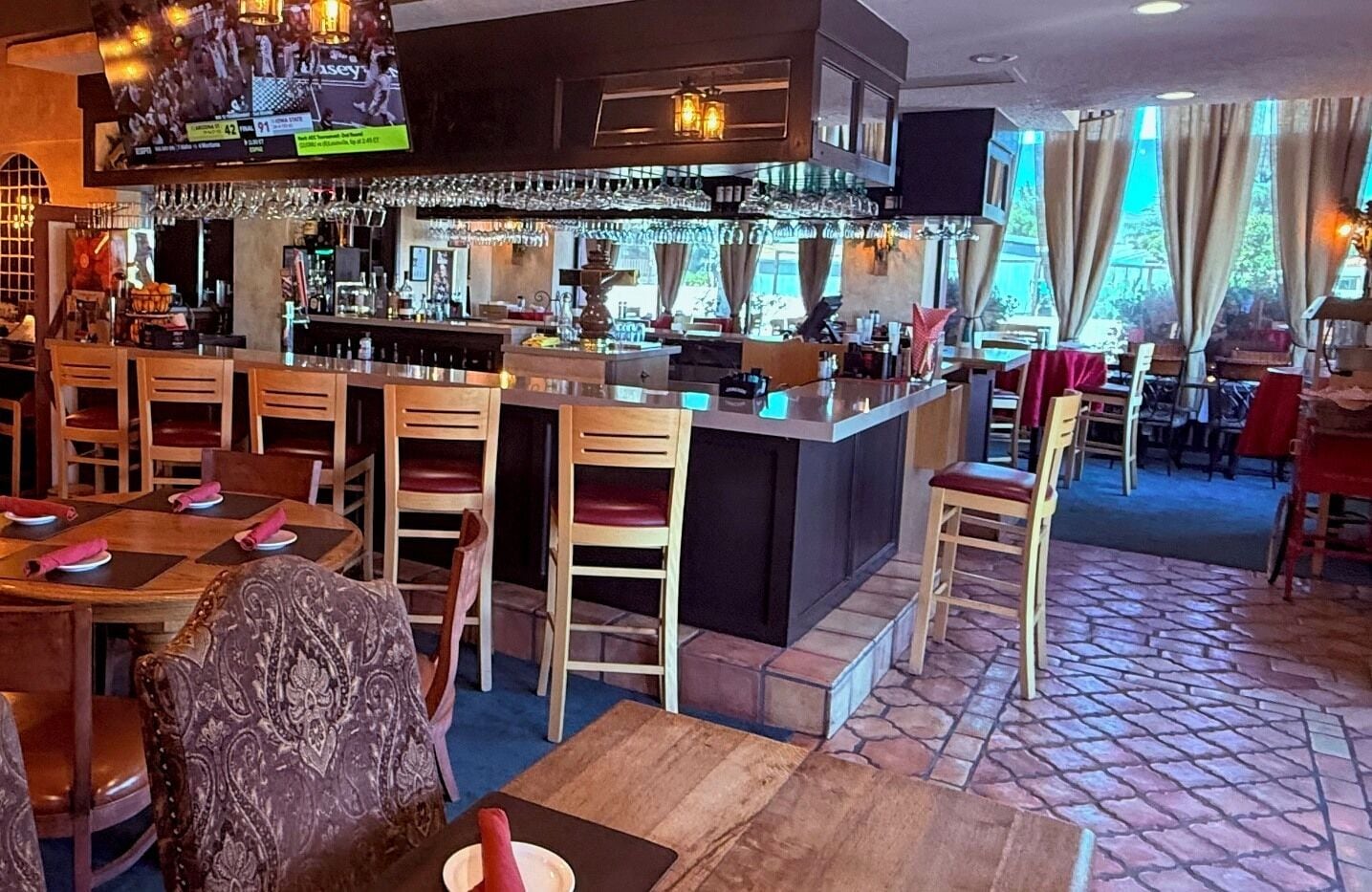 A restaurant with a bar area, wooden chairs, and a patterned tablecloth.
