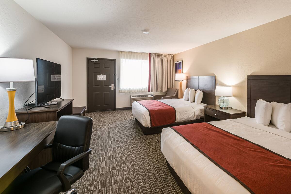 A hotel room with two beds, a desk with a computer, a chair, and a TV.