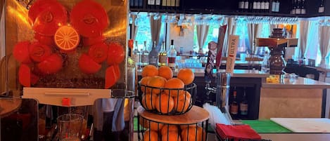 A bar area with a fruit press, a glass of orange juice, a basket of oranges, and a box of vodka.