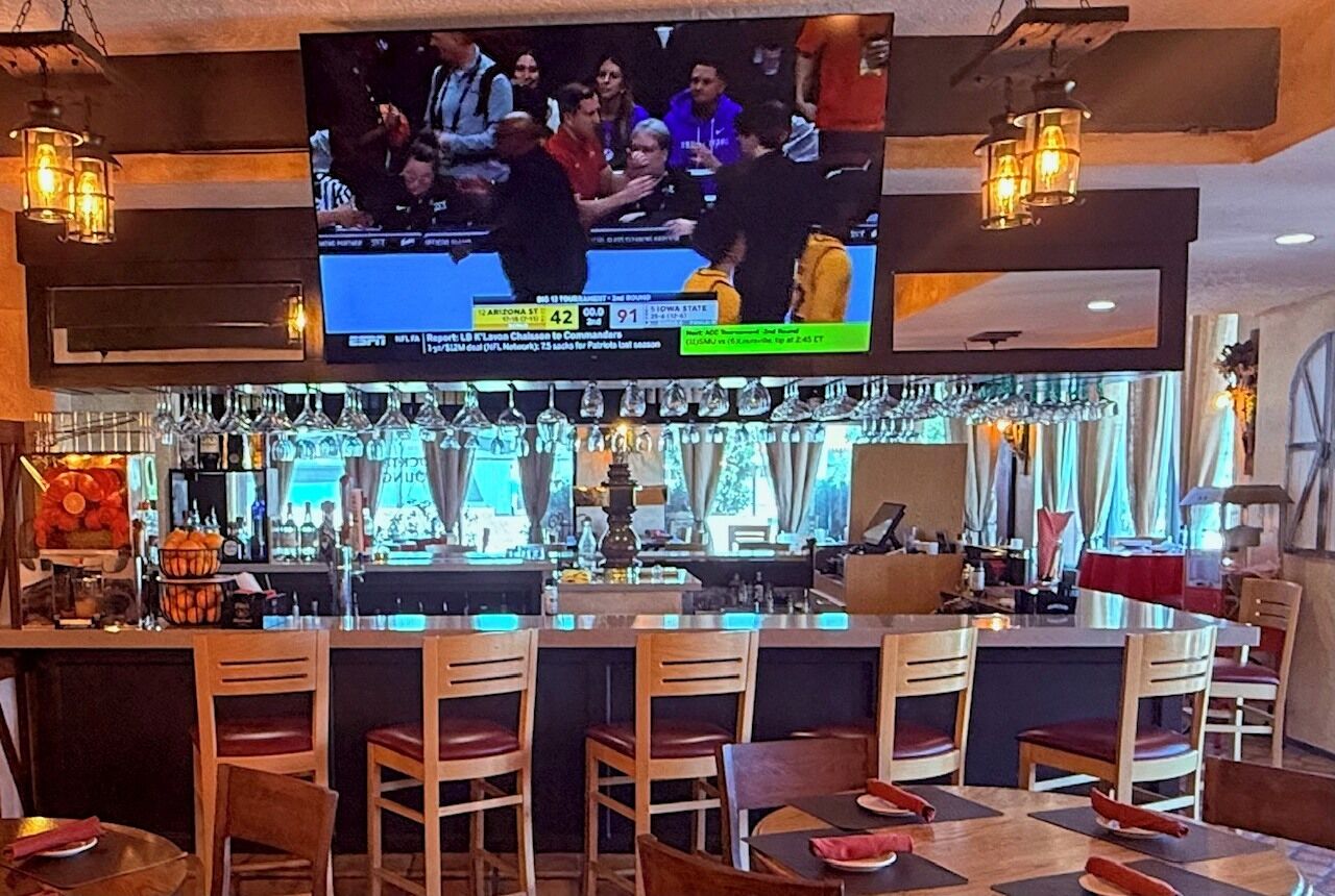 Zona de bar con diversas opciones de asientos, un televisor mostrando un evento deportivo y una barra con varios artículos.