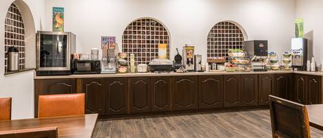 A breakfast bar with a microwave, coffee maker, and various food items.