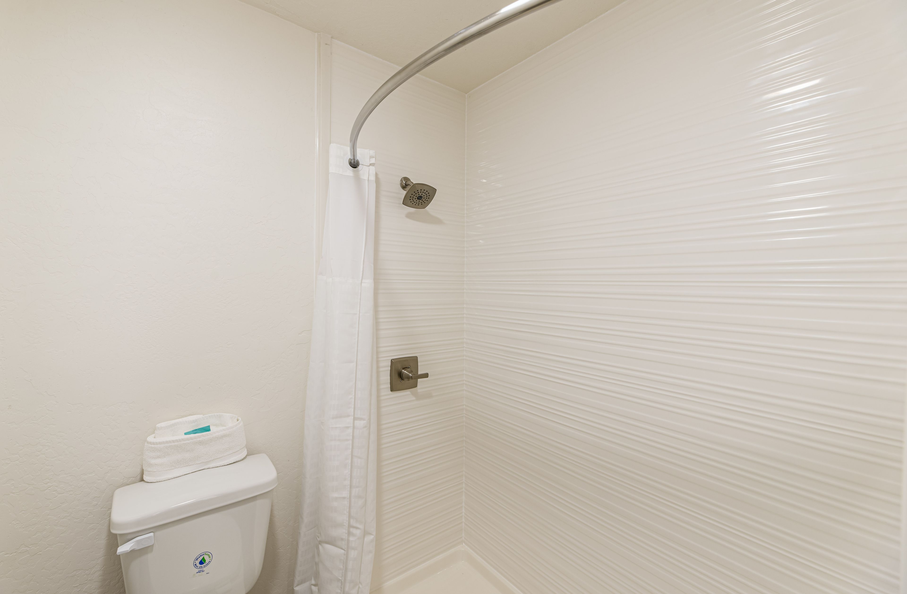 Un baño con inodoro blanco, ducha con puerta curva y pared de azulejos.