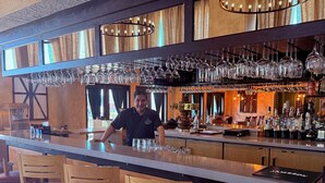 A bar area with a bartender, wooden chairs, and a bar counter with glasses and bottles. - Lux Verde Hotel (Cottonwood)
