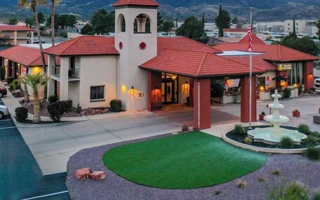 A hotel with a central tower, multiple red-roofed buildings, a landscaped courtyard with a fountain, and a mountainous backdrop.