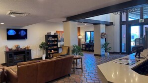 A lobby with a fireplace, a television, a bookshelf, a sofa, and a reception desk. - Lux Verde Hotel (Cottonwood)