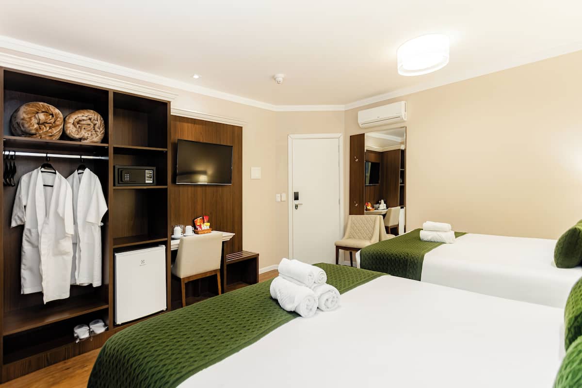 A hotel room with two beds, a wardrobe, a desk, a microwave, and a television.