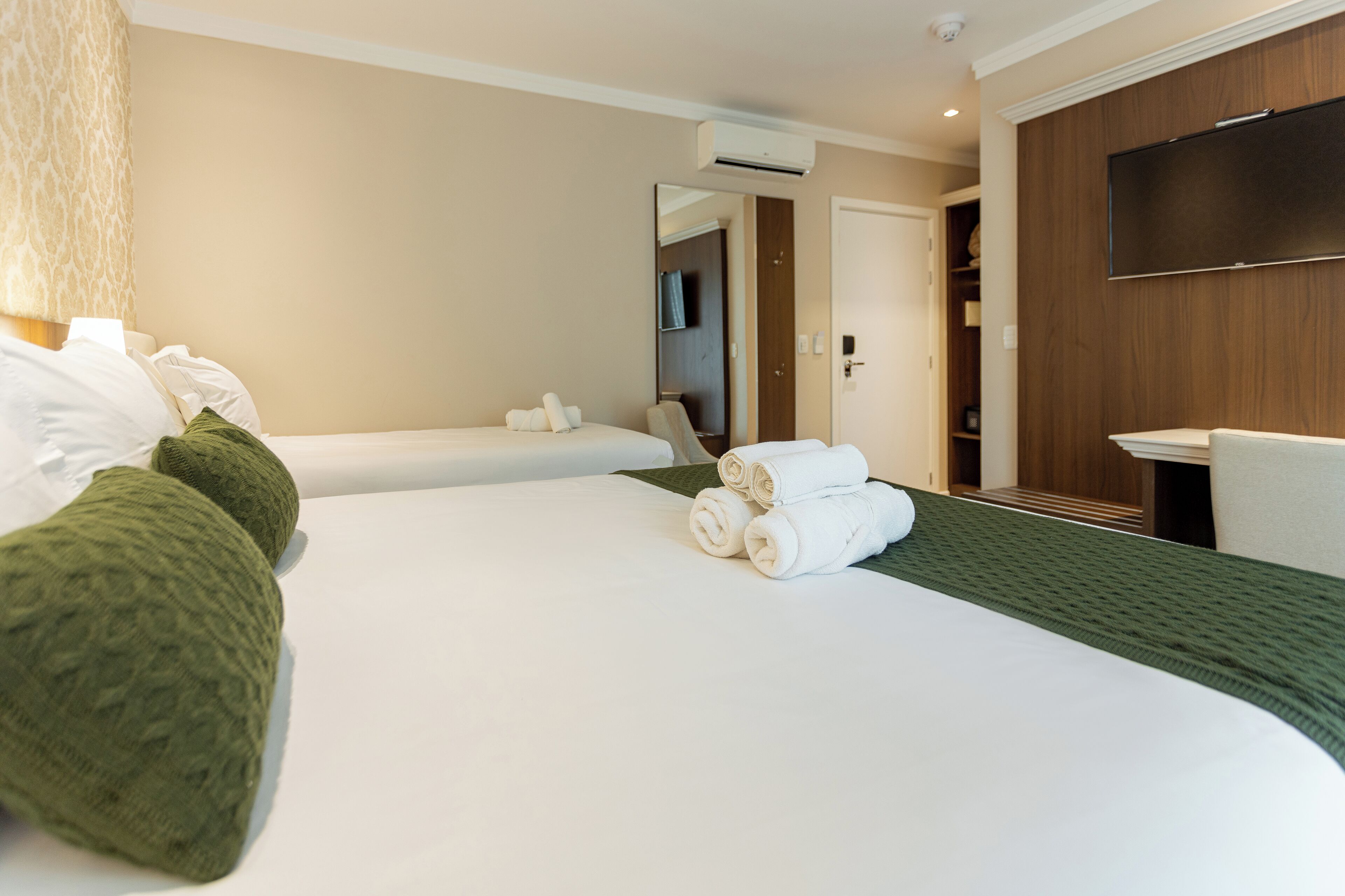 A hotel room with two beds, a TV, and a wooden panel wall.