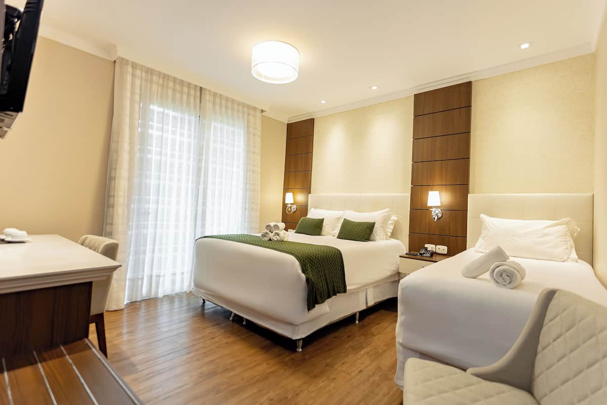 A hotel room with a large bed, a smaller bed, a desk, and a chair.