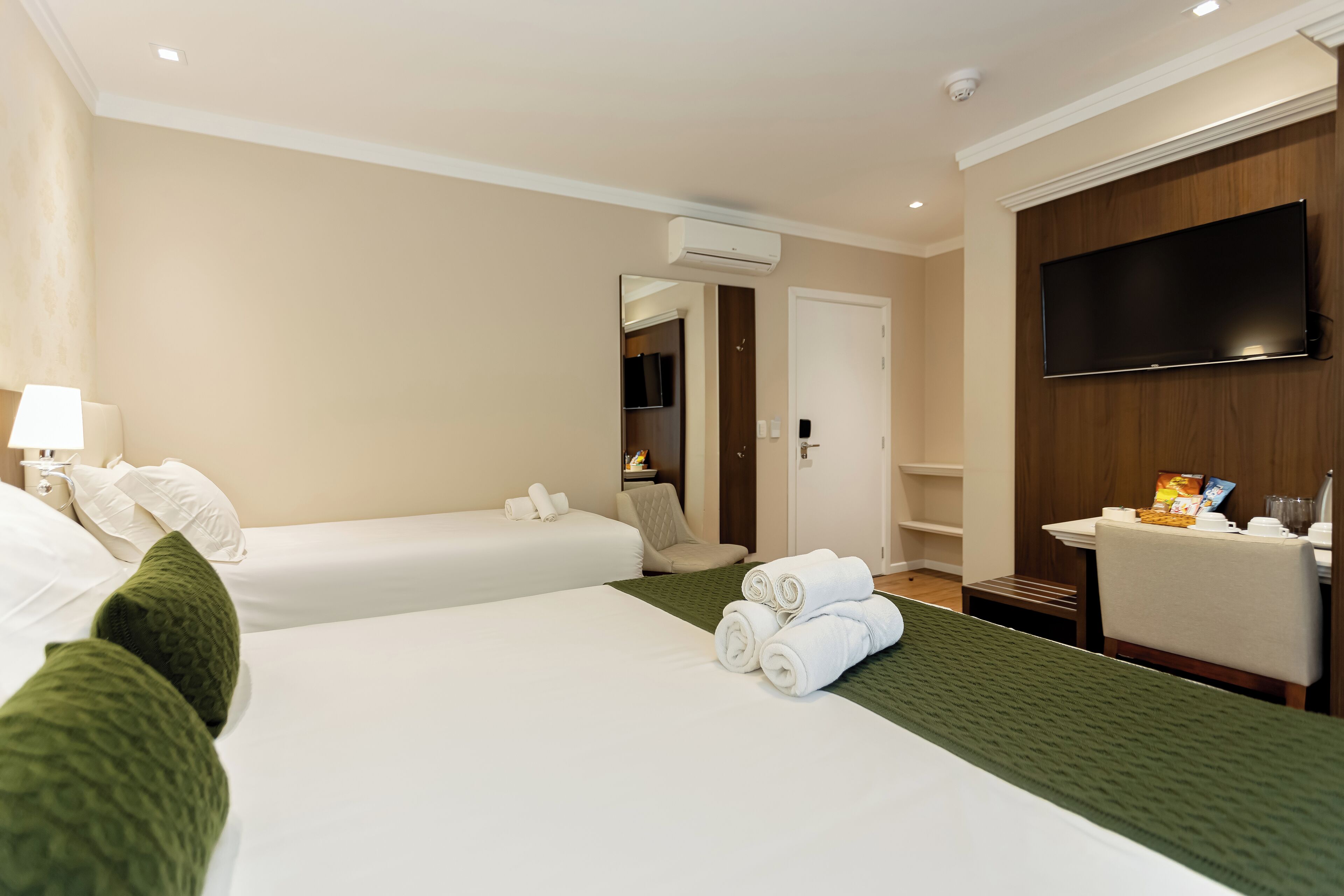 A hotel room with two beds, a flat-screen TV, a desk with a chair, and a small bathroom area.