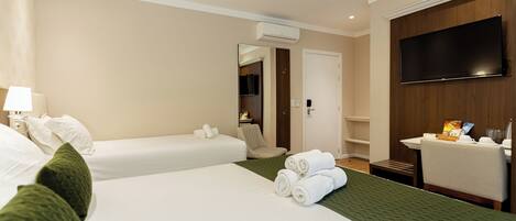A hotel room with two beds, a flat-screen TV, a desk with a chair, and a small bathroom area.