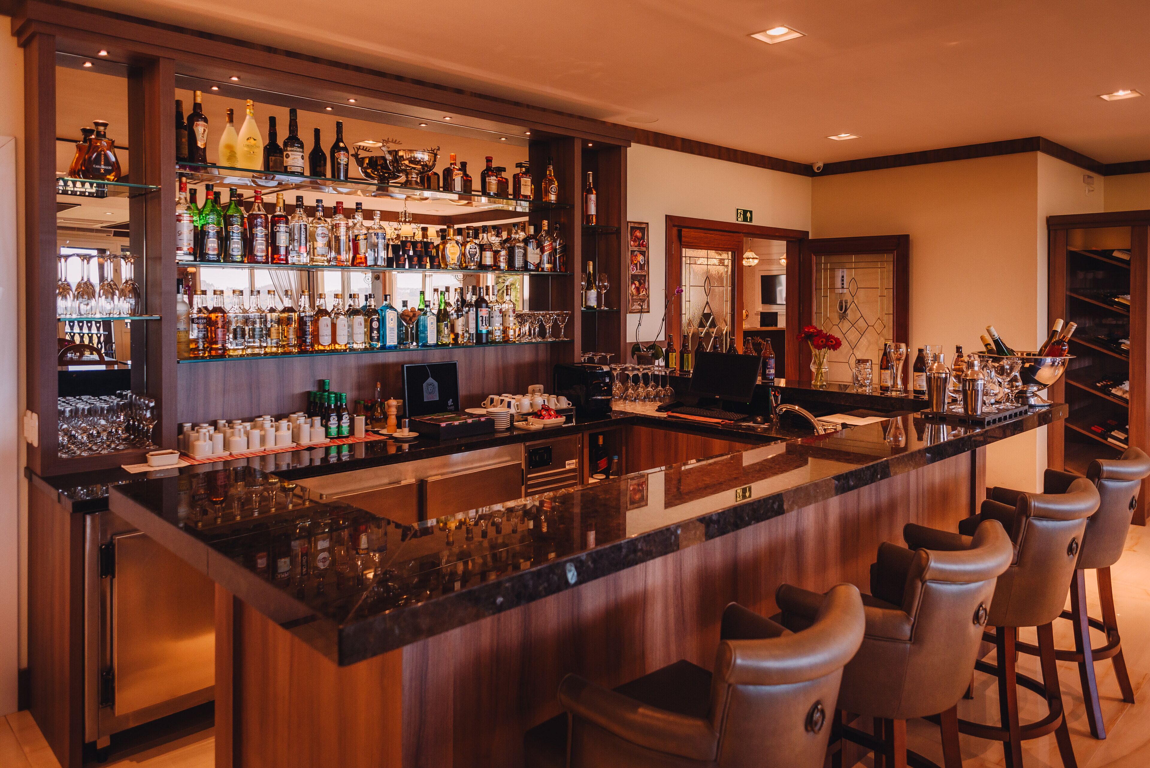 A bar area with a polished granite countertop, multiple bar stools, and a variety of liquor bottles and glasses.