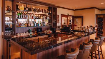 A bar area with a polished granite countertop, multiple bar stools, and a variety of liquor bottles and glasses.