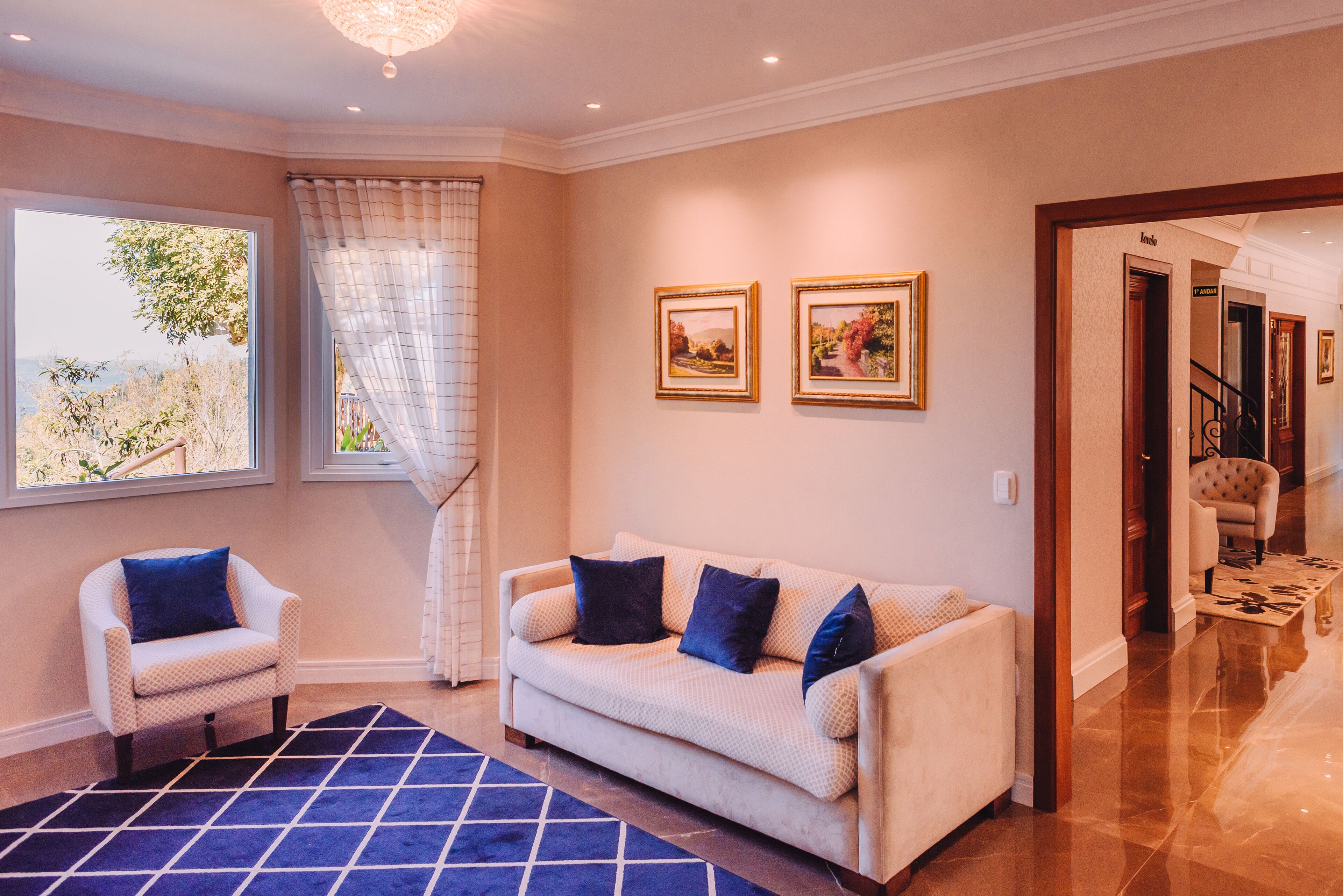 Una sala de estar con un sofá color beige, dos sillones, un tapete azul y dos cuadros en la pared.