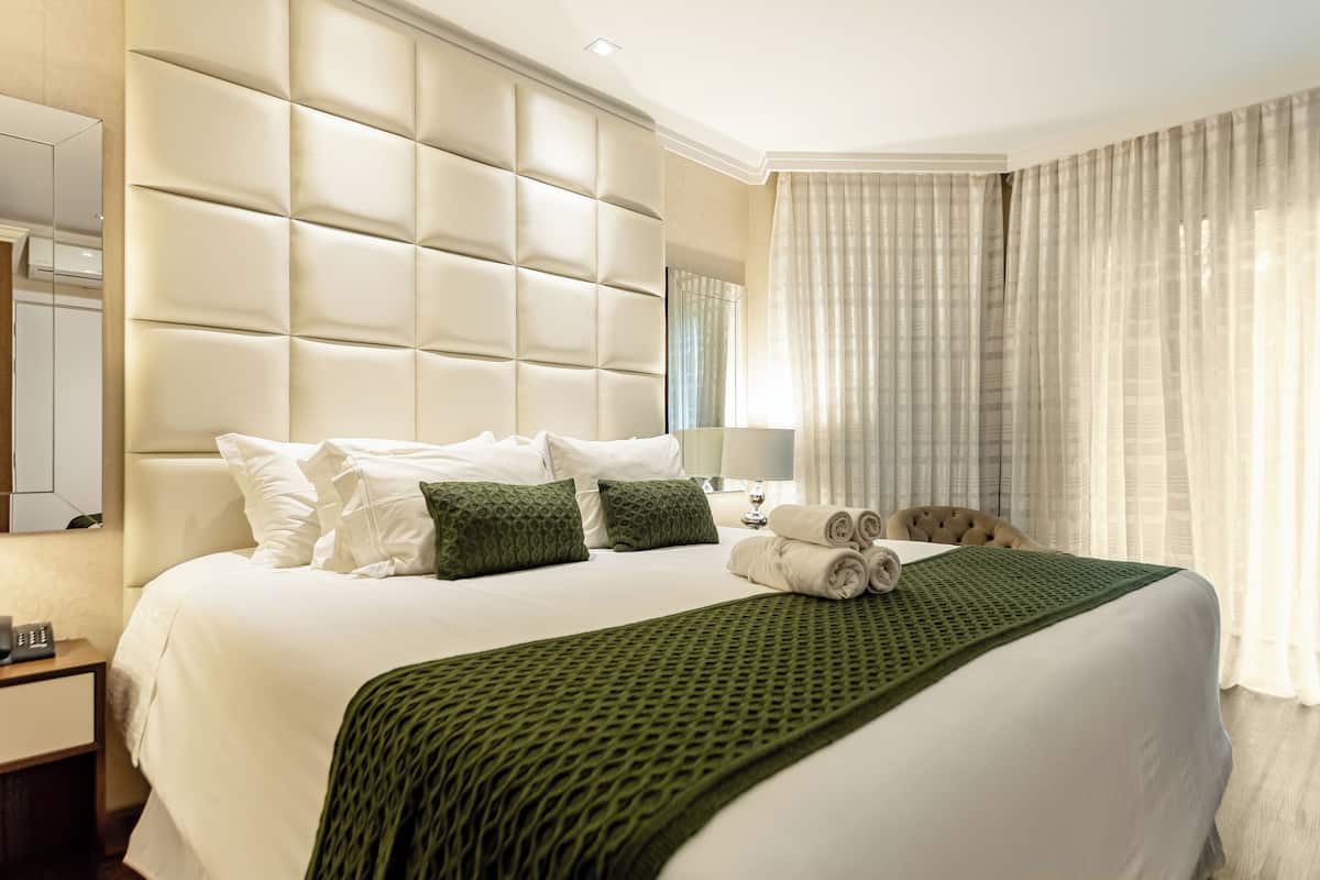 A hotel room with a large bed, a headboard, a bedside table, a lamp, and a window with curtains.