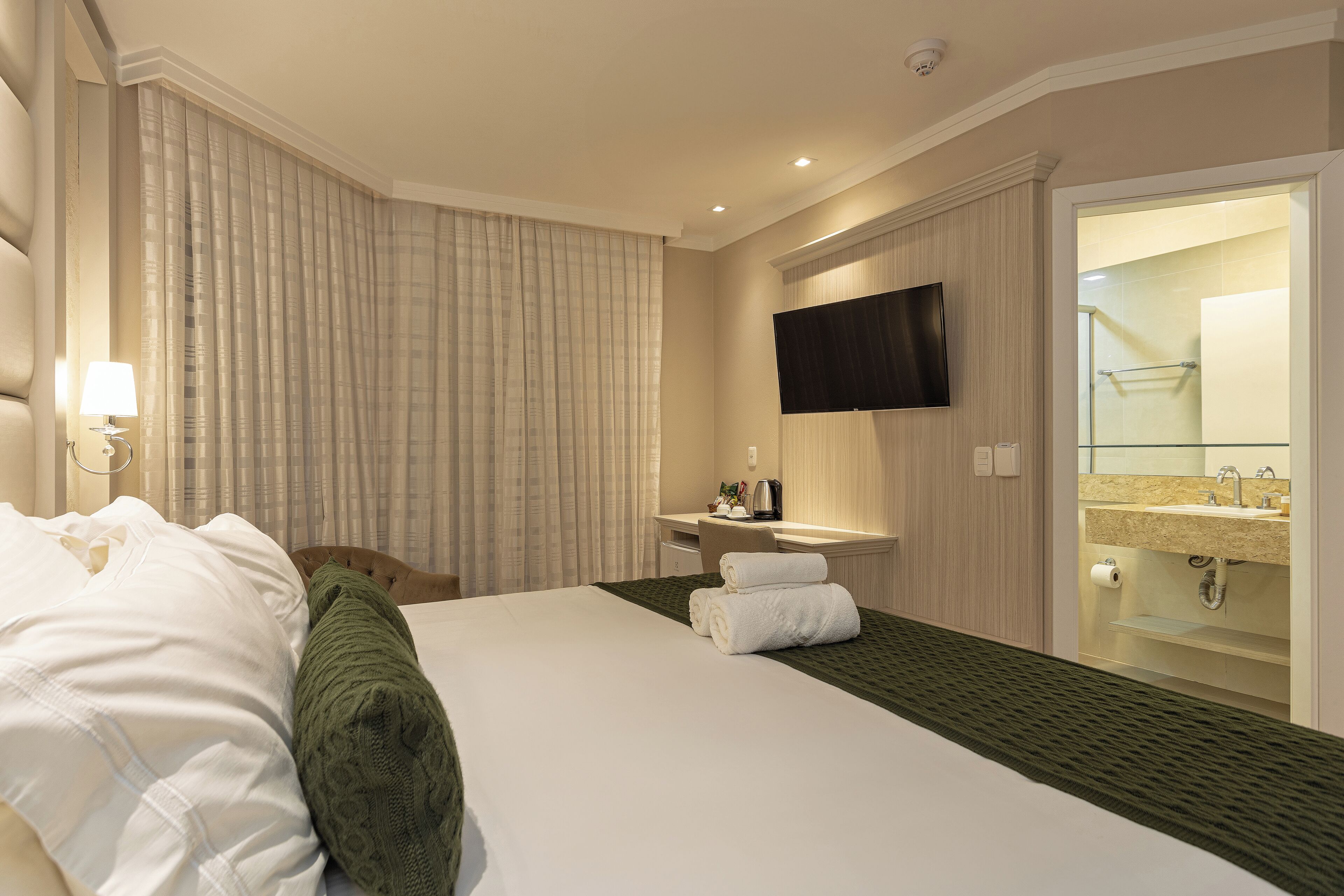 A hotel room with a bed, a desk, a TV, a bathroom with a sink and mirror.