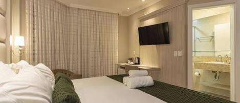 A hotel room with a bed, a desk, a TV, a bathroom with a sink and mirror.