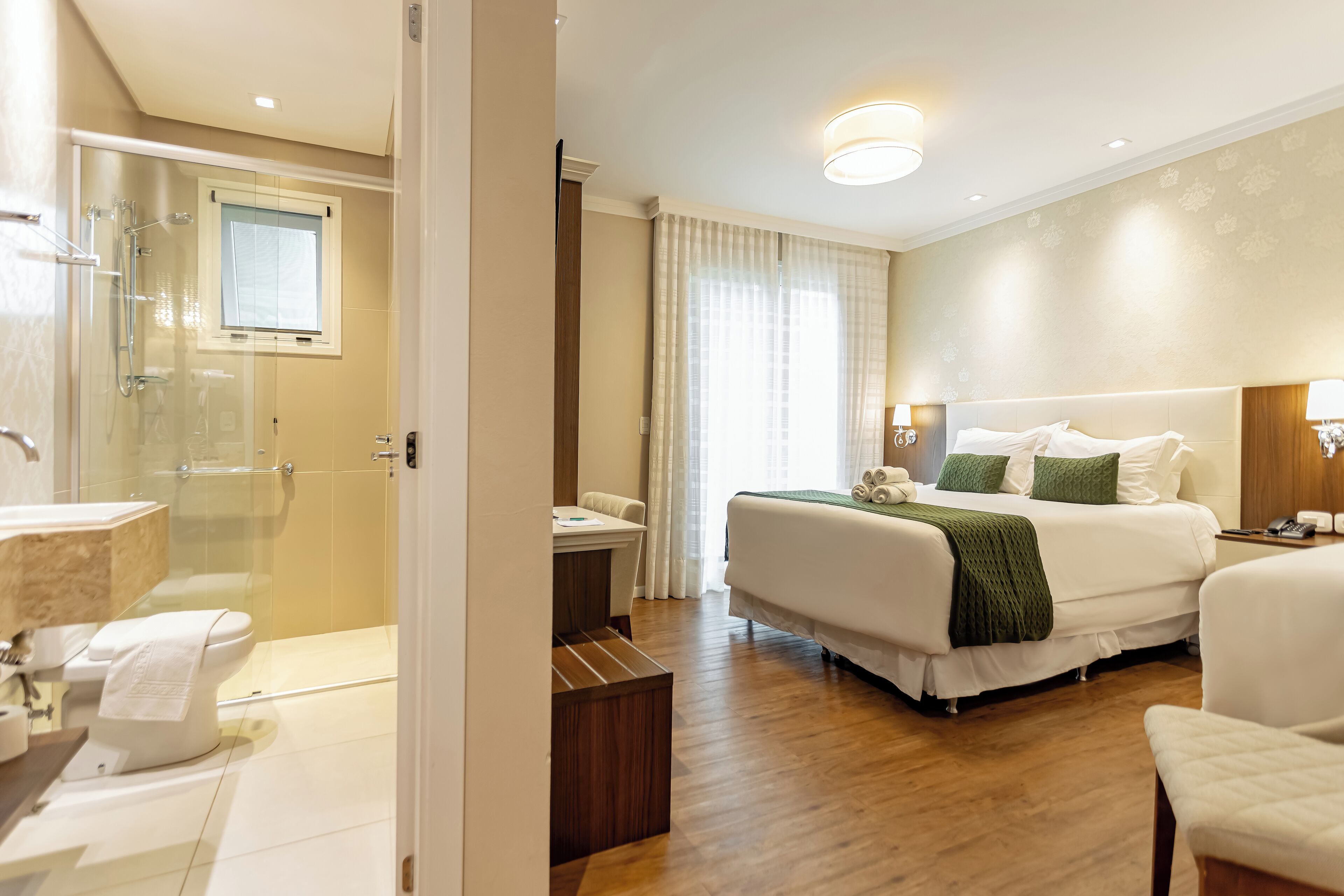 A hotel room with a bed, bedside table, lamp, and a view of the bathroom.