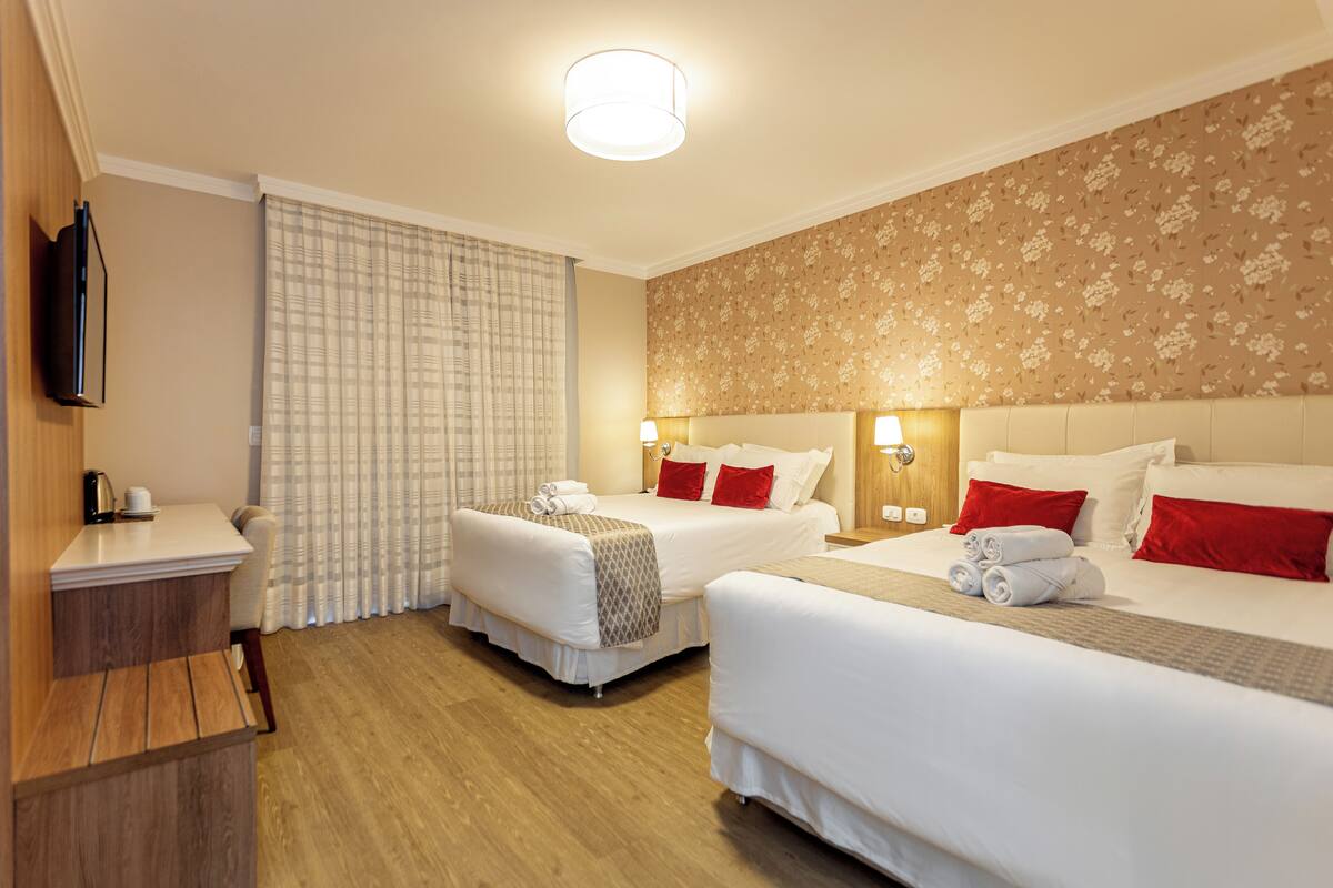 A hotel room with two beds, a desk, and a television.