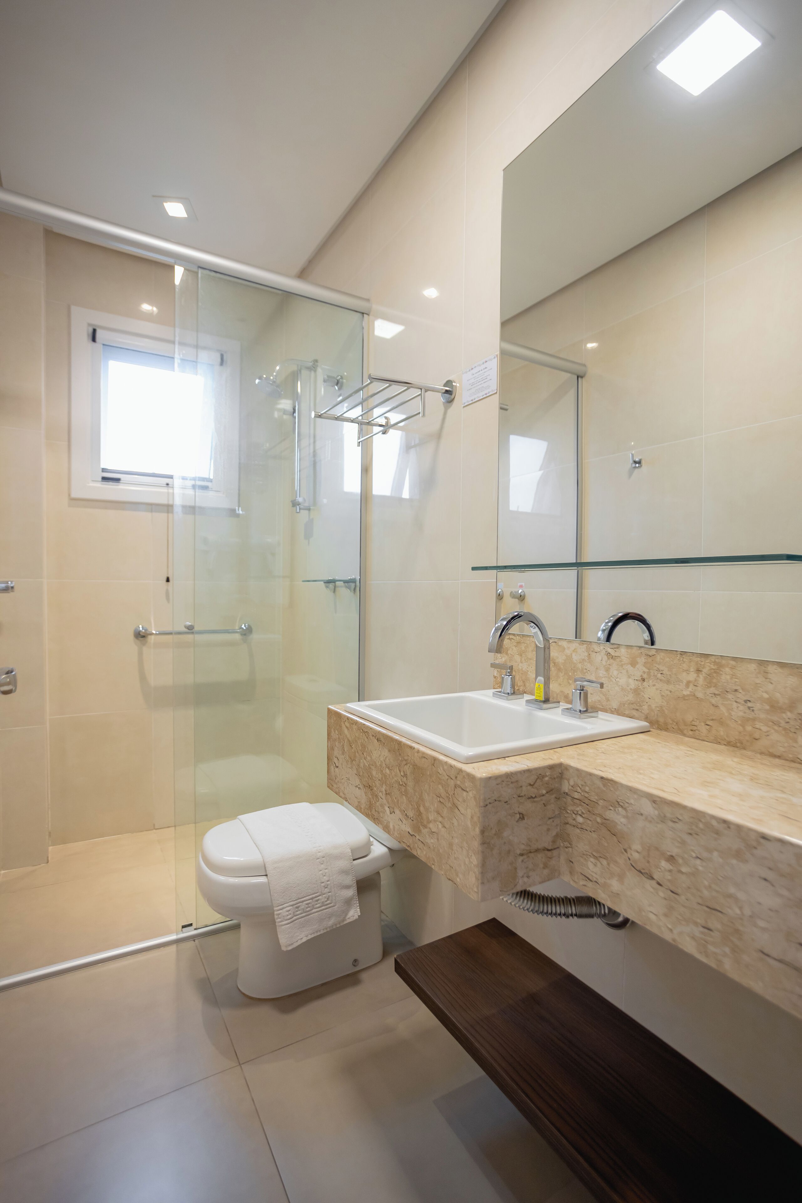 A modern bathroom with a glass-enclosed shower, a white toilet, a sink with a marble countertop, and a large mirror.