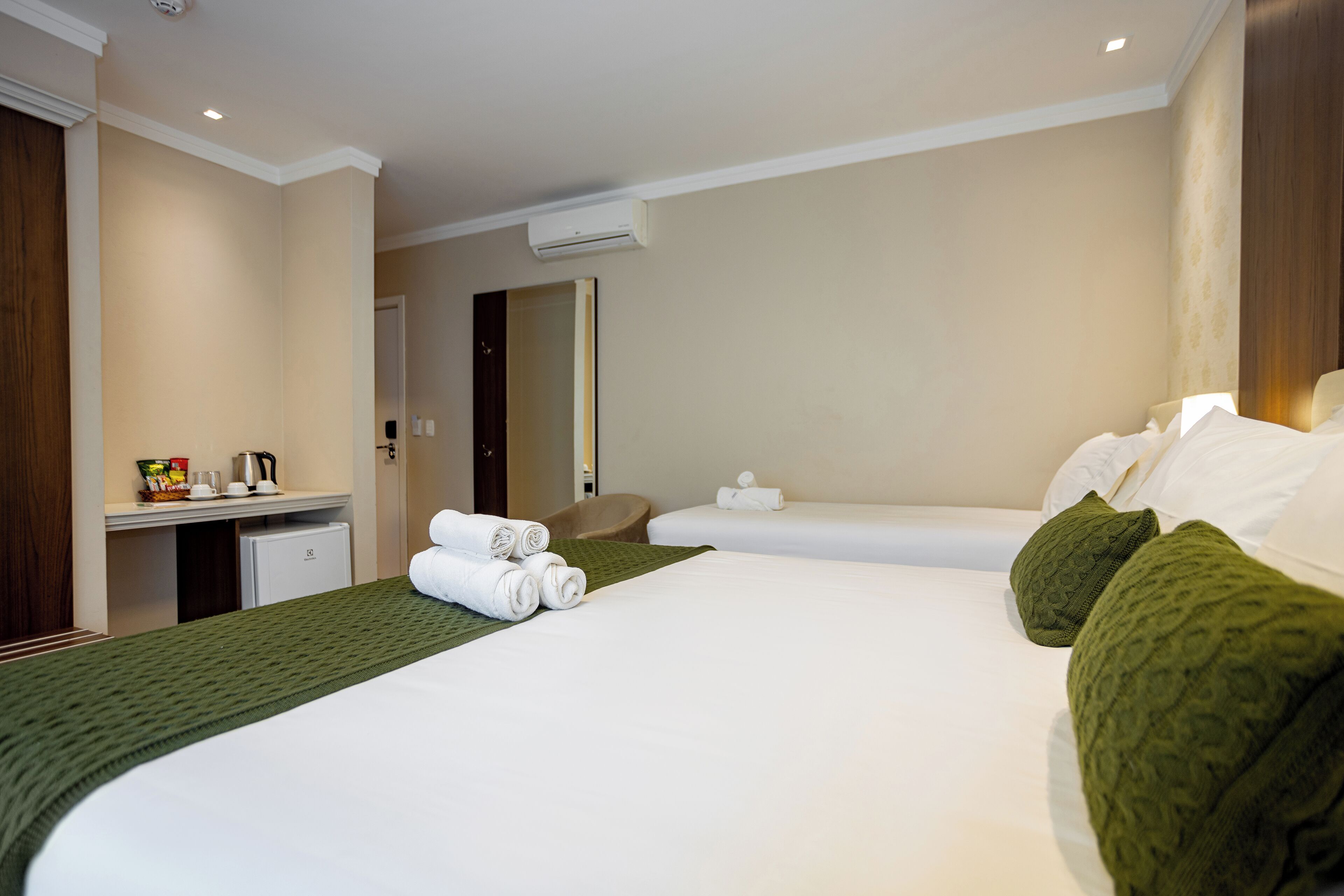Una habitación de hotel con una cama grande, dos camas más pequeñas, un escritorio con cafetera y un espejo.