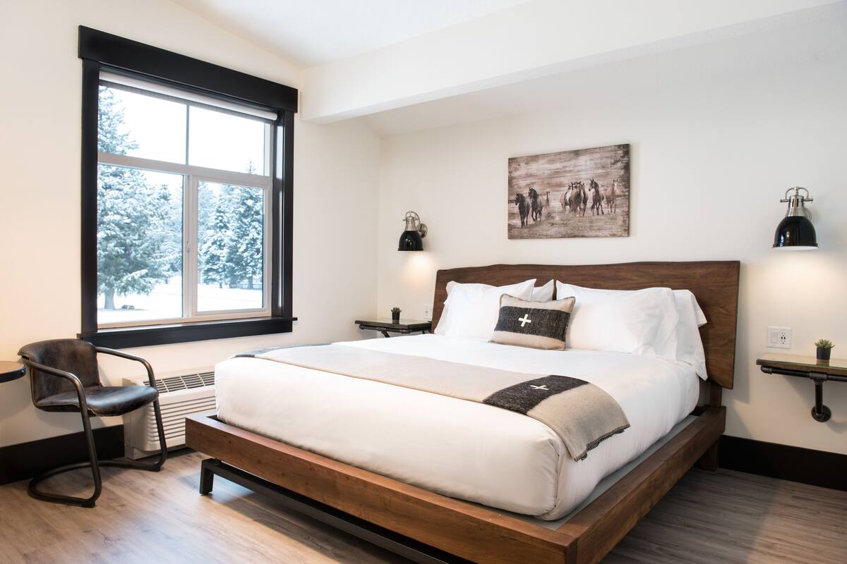 A bedroom with a large bed, a chair, a window, and a wall-mounted artwork.