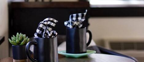 Two black mugs on a tray with a green coaster, a small potted plant, and a checkered cloth.