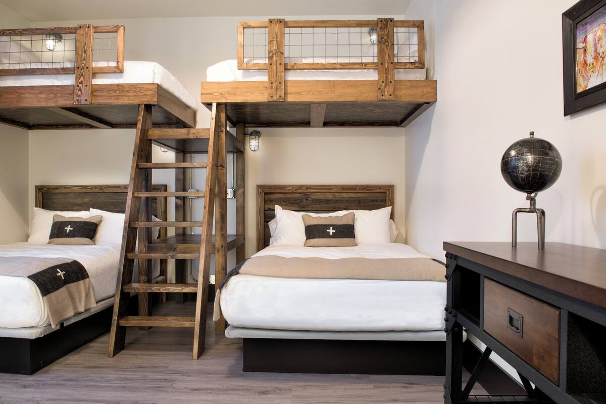 A room with two bunk beds, a ladder, a globe on a desk, and a framed picture on the wall.