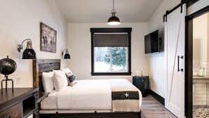 A bedroom with a bed, bedside lamps, a globe, a painting, a TV, and a sliding door. - Compass Rose Lodge (Huntsville)