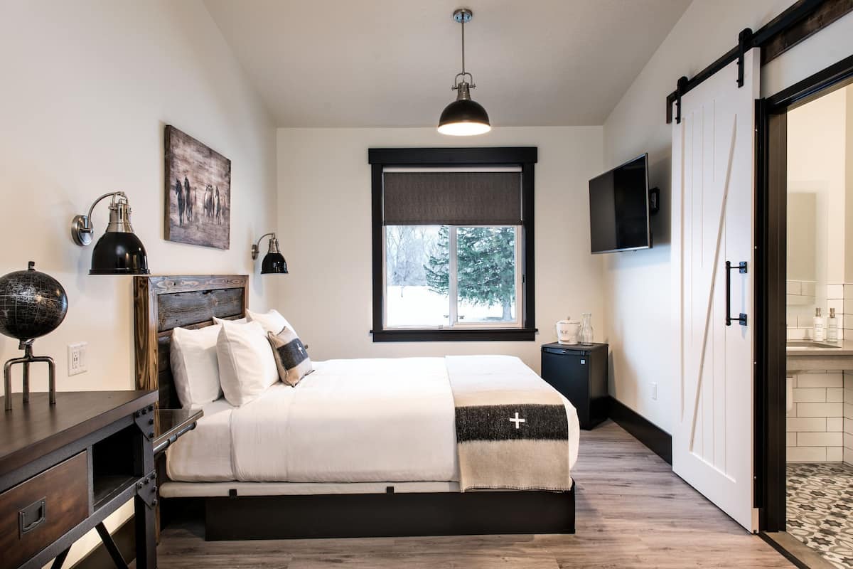A bedroom with a bed, bedside lamps, a globe, a painting, a TV, and a sliding door.