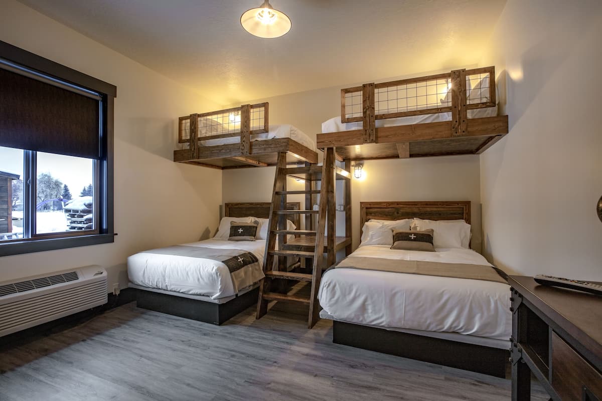 A room with bunk beds, a ladder, and a window with blinds.