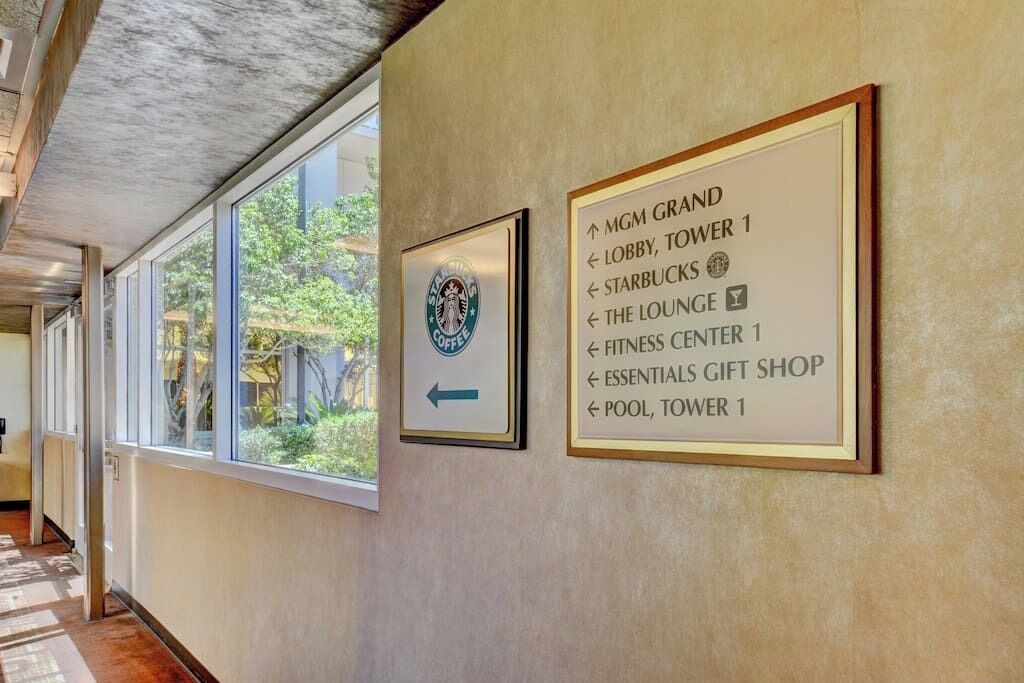 A hallway with directional signs to MGM Grand amenities including the lobby, tower 1, Starbucks, the lounge, fitness center, essentials gift shop, and pool, tower 1.