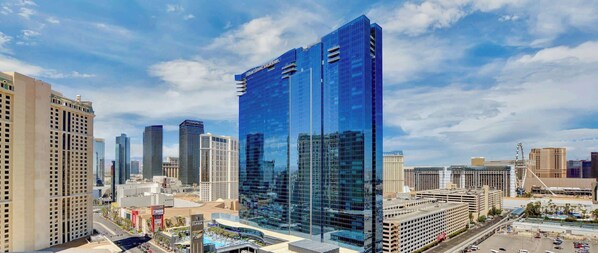 A modern high-rise hotel with a glass facade, surrounded by other high-rise buildings in a cityscape.