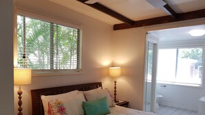 Une chambre à coucher comprenant un lit, deux lampes de chevet, une fenêtre avec des stores et une porte donnant sur un balcon.