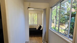 Un couloir étroit avec un plancher en bois, un banc noir et une fenêtre avec des rideaux.