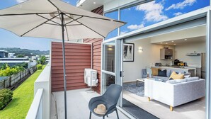 A balcony with a large umbrella, a chair, and a sofa. - Ocean Serenity Apartments Whitianga (Whitianga)