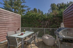 An outdoor patio with a table, chairs, a grill, and a view of trees.