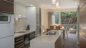 A modern kitchen with a central island, built-in appliances, and a view to a balcony. - Ocean Serenity Apartments Whitianga (Whitianga)