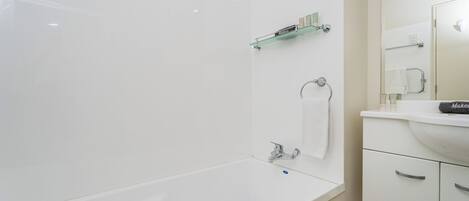 A modern bathroom with a white bathtub, a glass shelf with toiletries, a towel rack, and a vanity with a mirror.