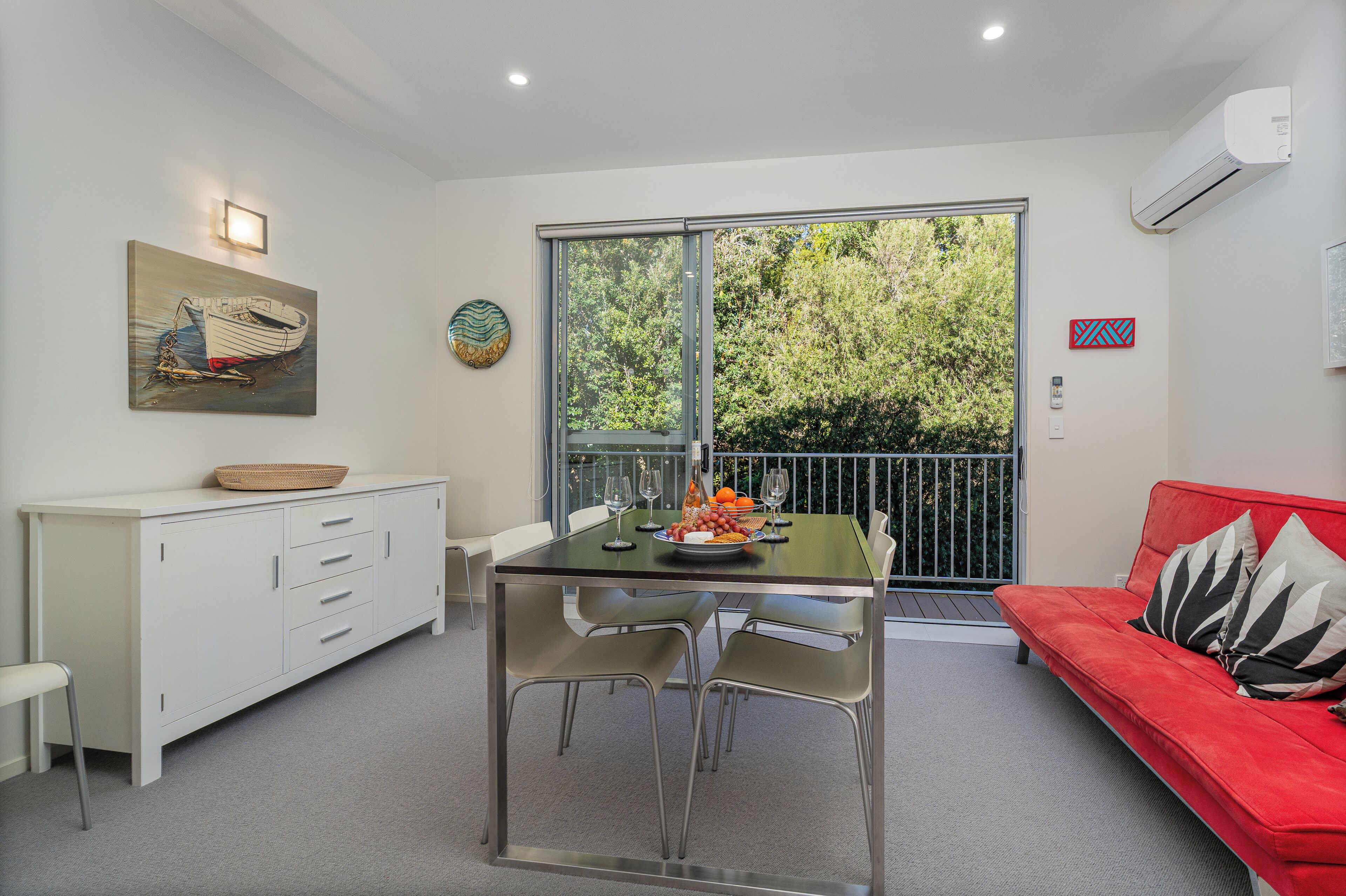 A dining area with a table set for two, a red sofa, and a white cabinet.