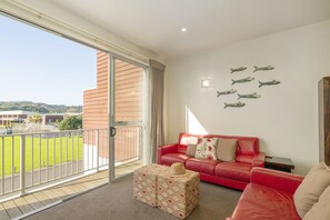 A balcony with a red leather sofa, a patterned ottoman, and decorative fish wall art.