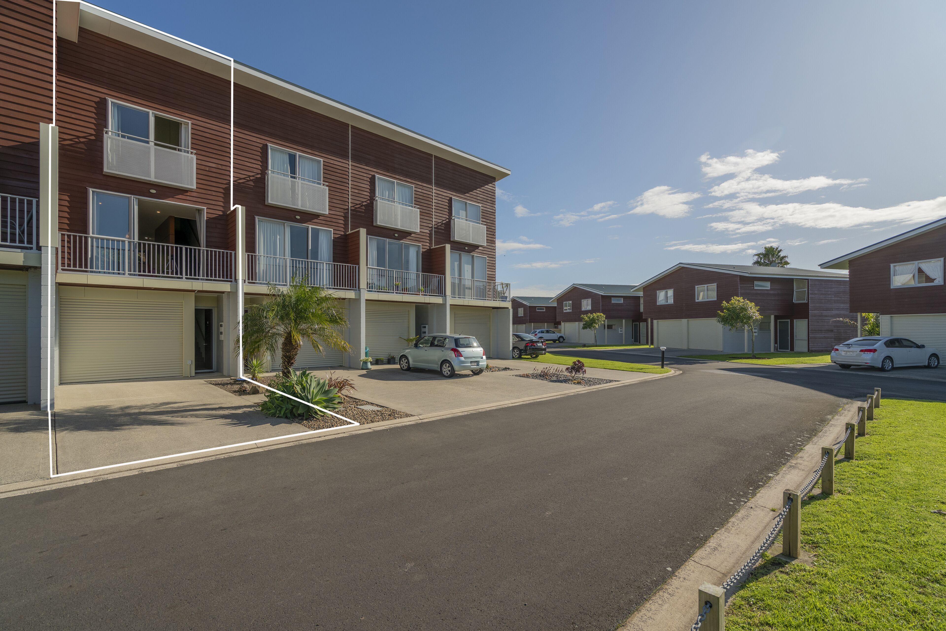 A modern apartment complex with multiple units, a gated driveway, and a clear sky.