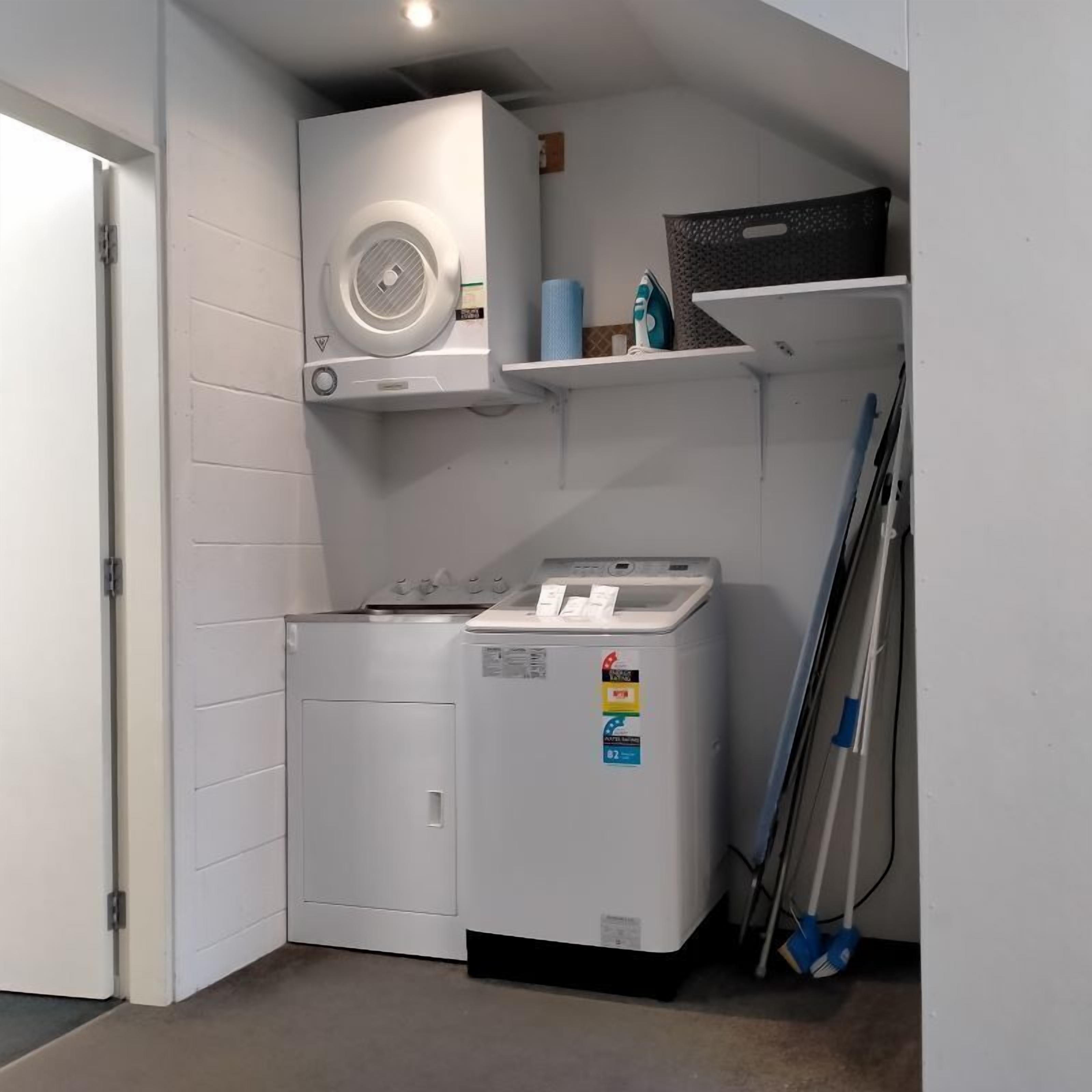 Une buanderie équipée d’un lave-linge et d’un sèche-linge, d’un ventilateur de plafond et d’une serpillière posée sur le sol.
