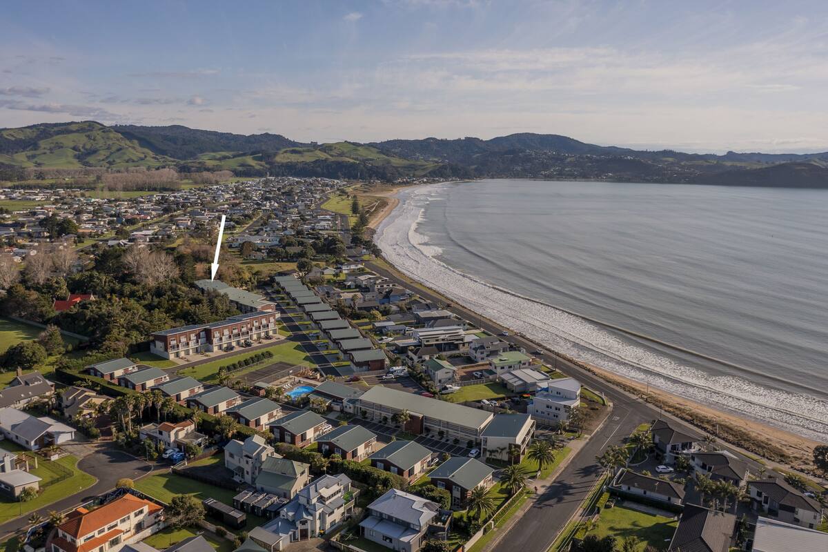 Une zone résidentielle côtière avec des maisons le long de la plage, un ciel dégagé et des collines en arrière-plan.