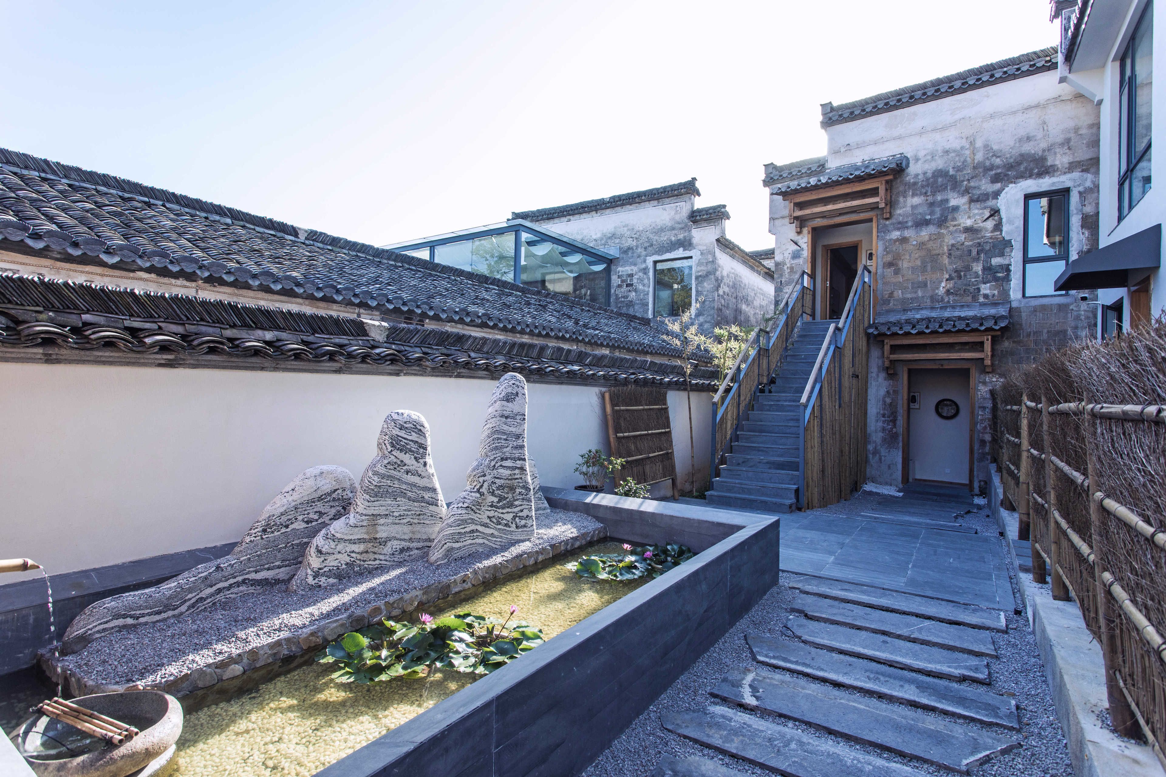 A traditional courtyard with stone sculptures, a koi pond, and a wooden staircase leading to a door.