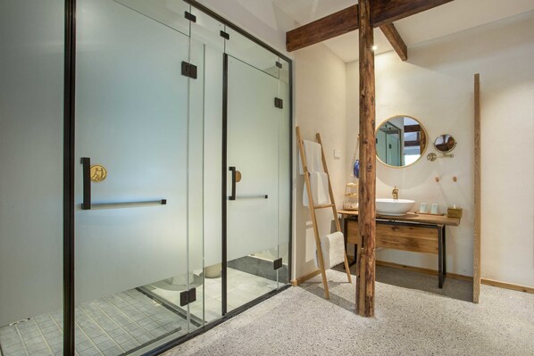 Un baño moderno con cabina de ducha de vidrio, un mueble de tocador de madera con lavamanos y un espejo en la pared.