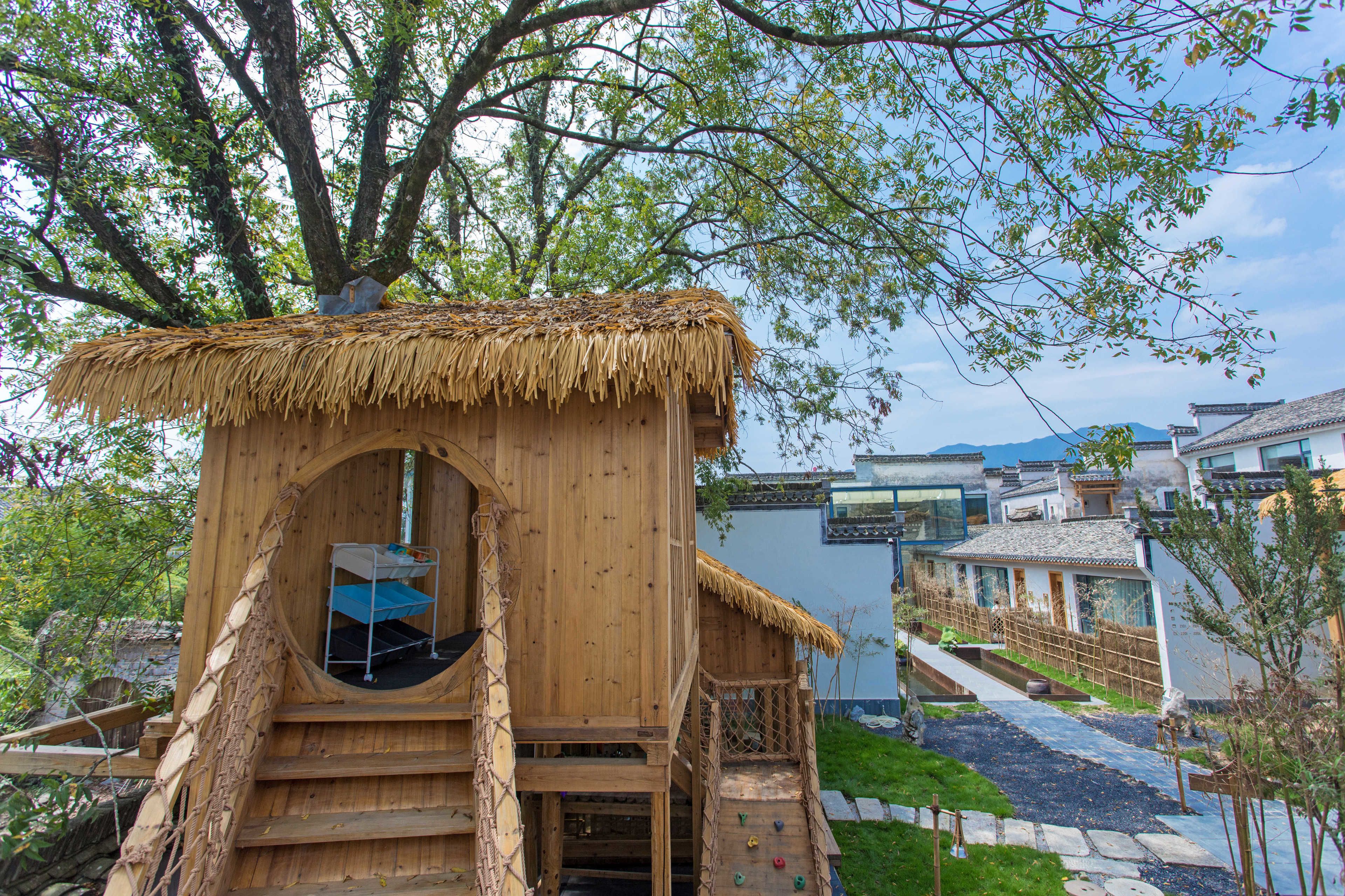 A wooden treehouse with a thatched roof, a ladder, and a small window.